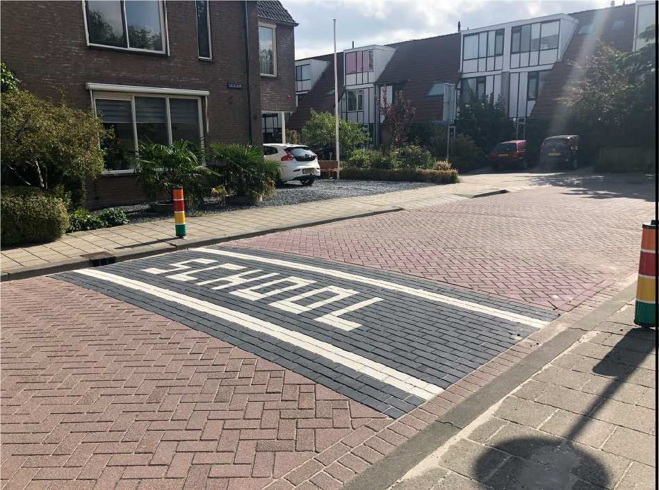 Foto van een schoolzone met daarop twee lage regenboogpalen en de tekst 'school' op het wegdek.