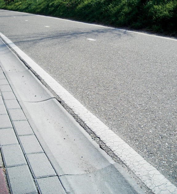 De foto toont een molgoot. Dat is een goot tussen de rijweg en het trottoir. De molgoot zorgt ervoor dat hemelwater wordt afgevoerd en maakt de weg optisch smaller