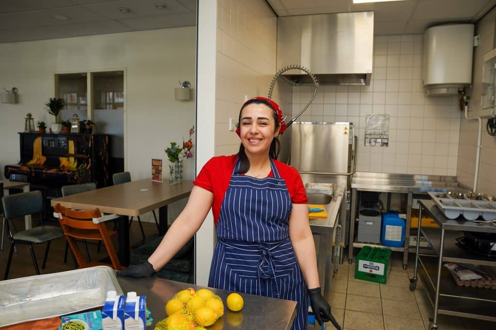 Foto van azc-bewoonster Walaa. Ze staat in de keuken van buurthuis De Walvis en draagt een schort en keukenhandschoenen. Voor haar liggen citroenen.