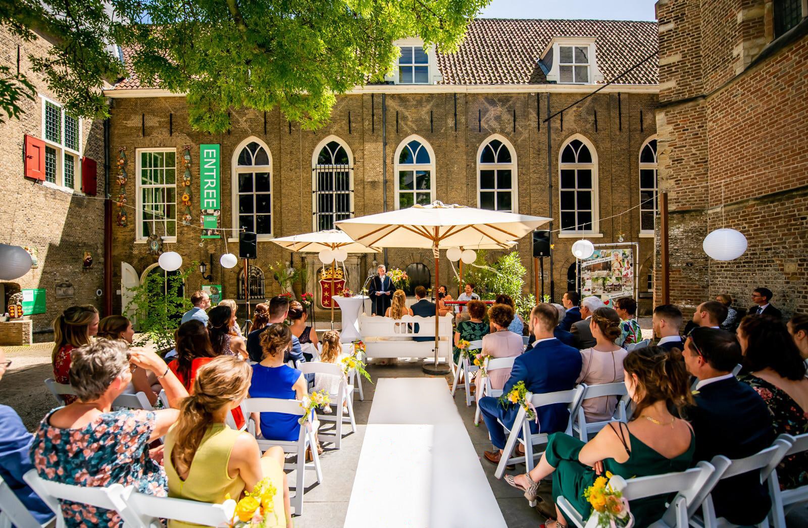 Terras van het Museumcafé Gouda. Op de foto zijn een witte loper te zien, publiek aan beide kanten en aan het eind van de loper een bruidspaar met trouwambtenaar.